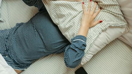 Frau liegt mit Pyjama im Bett und hält sich ein Kissen auf das Gesicht. 