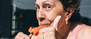 Eine ältere Dame isst eine Wassermelone und zeigt einen Daumen nach oben.