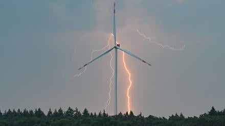 Blitze eines Gewitters leuchten über der Landschaft mit einer Windenergieanlage in Brandenburg. 