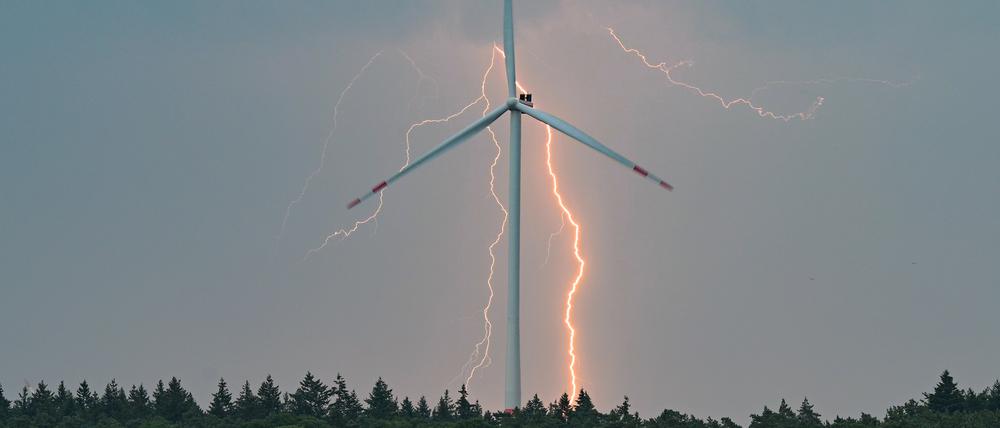 Blitze eines Gewitters leuchten über der Landschaft mit einer Windenergieanlage in Brandenburg. 