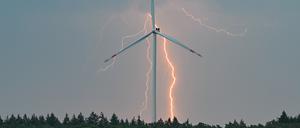 Blitze eines Gewitters leuchten über der Landschaft mit einer Windenergieanlage in Brandenburg. 