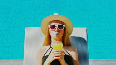 Summer portrait of happy relaxing young woman lying on a deckchair with cup of juice on a pool background