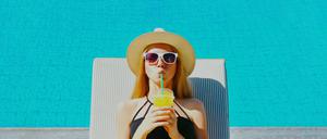 Summer portrait of happy relaxing young woman lying on a deckchair with cup of juice on a pool background