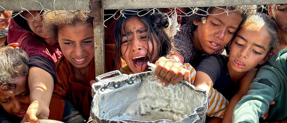 Palästinensische Kinder versuchen im Gebiet Al-Mawasi im Gazastreifen, mit ihren Töpfen Nahrungsmittel zu bekommen, die von Wohltätigkeitsorganisationen verteilt werden.