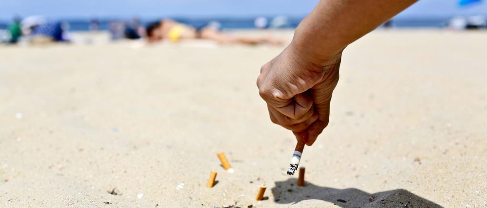 Ein Mann drückt einen Zigarettenstummel am Strand aus.