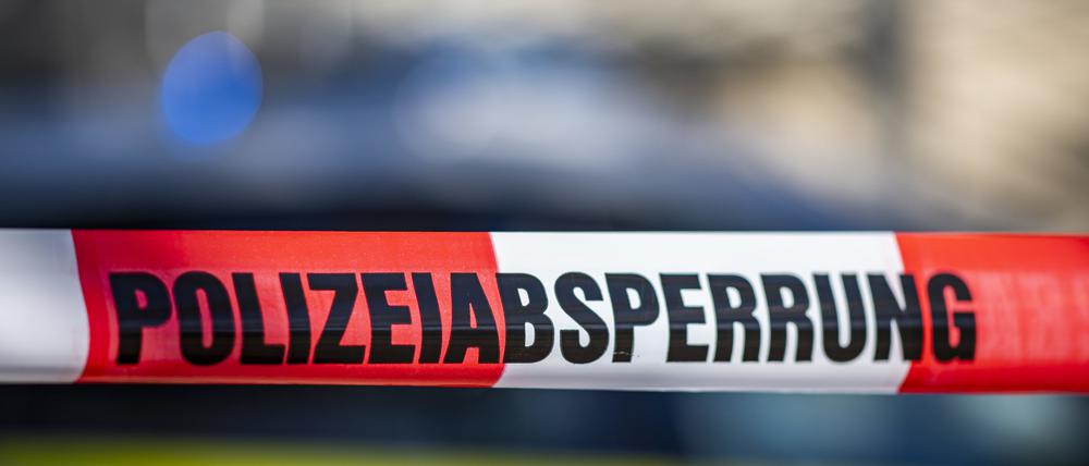 Ein Absperrband mit der Aufschrift „Polizeiabsperrung“ ist vor einem Polizeiwagen aufgespannt. (Symbolbild)