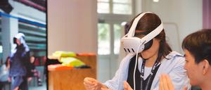 Frau mit Virtual-Reality-Brille steht vor einem Bildschirm.