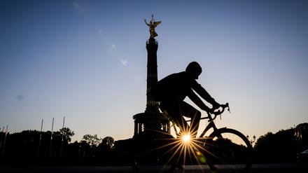 Die Sonne geht neben der Siegessäule auf, während ein Fahrradfahrer vorbeifährt.