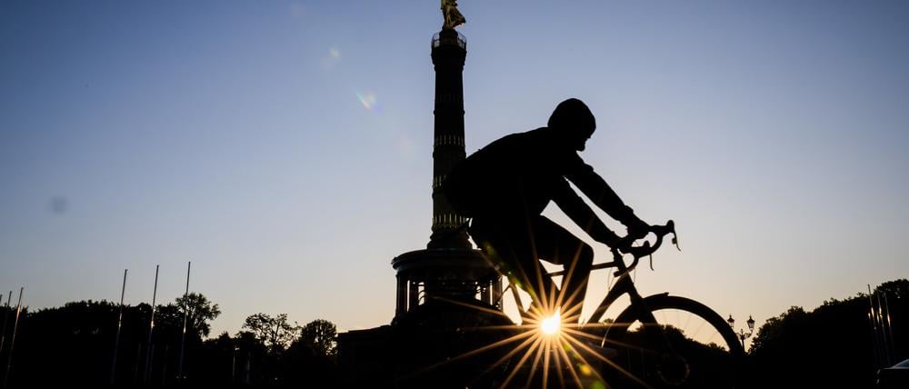 Die Sonne geht neben der Siegessäule auf, während ein Fahrradfahrer vorbeifährt.