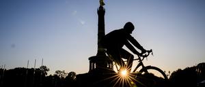 Die Sonne geht neben der Siegessäule auf, während ein Fahrradfahrer vorbeifährt.