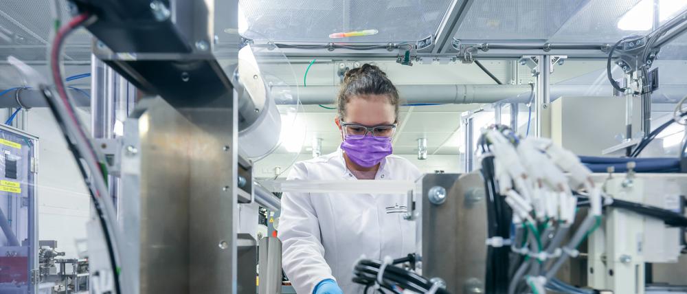 Eine junge Chemie-Laborantin mit Mundschutz und im weißen Kittel arbeitet in einem Labor an elektrochemischen Energiespeichern.