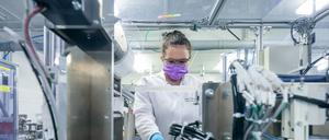 Eine junge Chemie-Laborantin mit Mundschutz und im weißen Kittel arbeitet in einem Labor an elektrochemischen Energiespeichern. 