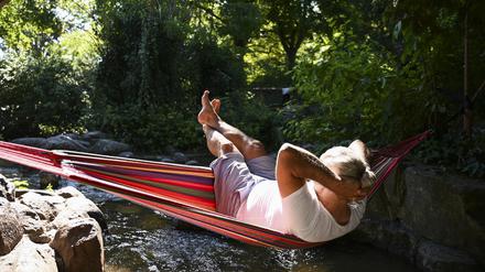 Ein Mann schaukelt im Viktoriapark auf dem Kreuzberg in einer Hängematte über dem Wasser. 