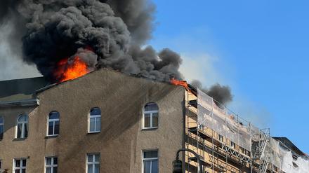 Aus dem Dachgeschoss eines Mehrfamilienhauses in Berlin-Schöneberg brechen Flammen hervor und es bildet sich eine dunkle Rauchwolke darüber. 