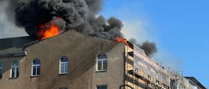 Aus dem Dachgeschoss eines Mehrfamilienhauses in Berlin-Schöneberg brechen Flammen hervor und es bildet sich eine dunkle Rauchwolke darüber. 