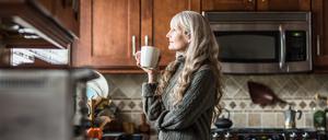 Eine Frau trinkt in ihrer Küche Kaffee. 