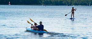 Paddler in einem Boot und eine Frau auf einem Stand-Up-Paddle-Brett sind auf dem Müggelsee.