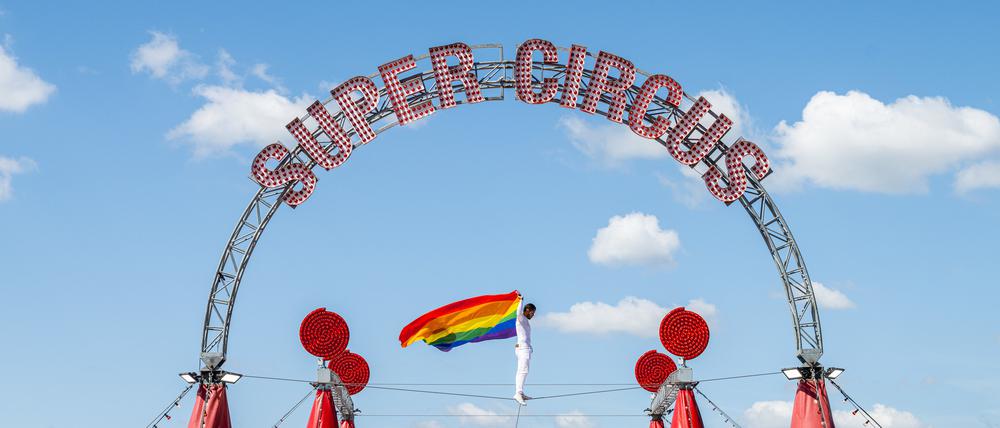04.07.2025, Nordrhein-Westfalen, Bielefeld: Der Hochseilartist David Ruiz vom Zirkus Charles Knie balanciert auf einem Seil über dem Zirkuszelt, wo eine Regenbogenfahne aus Protest hängt. Der Zirkus will aus Protest gegen die Haltung von Bundeskanzler Merz und Bundestagspräsidentin Klöckner (beide CDU) die Regenbogenfahne auf dem Zirkuszelt hissen. (zu dpa: «Zirkus hisst Regenbogenfahne aus Protest gegen Merz») Foto: Guido Kirchner/dpa +++ dpa-Bildfunk +++