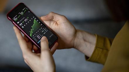 Hände halten ein Smartphone, auf dem ein Aktienchart abgebildet ist.