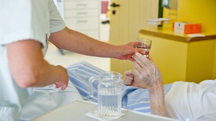 Eine Krankenpflegerin reicht einem Patienten ein Glas Wasser (Symbolbild).