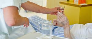 Eine Krankenpflegerin reicht einem Patienten ein Glas Wasser (Symbolbild).