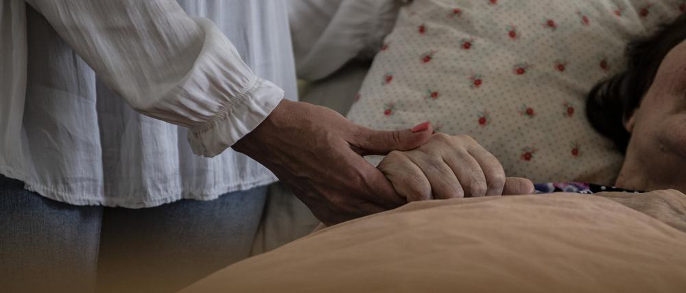 In einem Pflegeheim hält eine Frau die Hand einer Pflegebedürftigen.