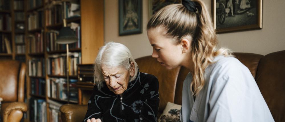 Pflege und Hilfen zu hause statt im Heim: eine alte Frau im Gespräch mit einer Betreuerin im Wohnzimmer.