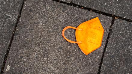 Ein gebrauchter orangefarbener Mund-Nasen-Schutz liegt auf dem Gehweg. 