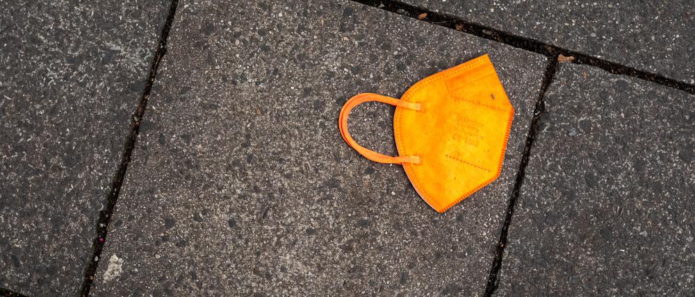 Ein gebrauchter orangefarbener Mund-Nasen-Schutz liegt auf dem Gehweg. 