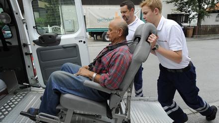 Das Archivfoto zeigt einen Freiwilligendienstleistenden, der beim Roten Kreuz gezeigt bekommt, wie man einen Gehbehinderten richtig in einen Transporter schiebt.