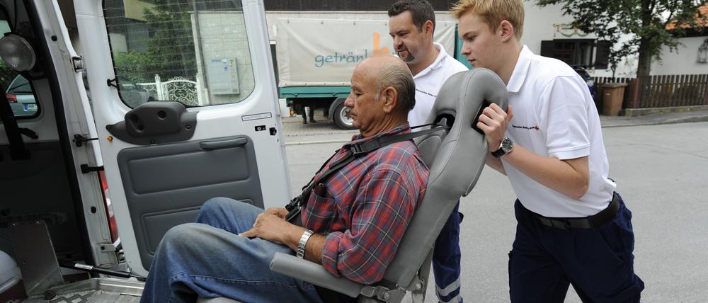 Das Archivfoto zeigt einen Freiwilligendienstleistenden, der beim Roten Kreuz gezeigt bekommt, wie man einen Gehbehinderten richtig in einen Transporter schiebt.
