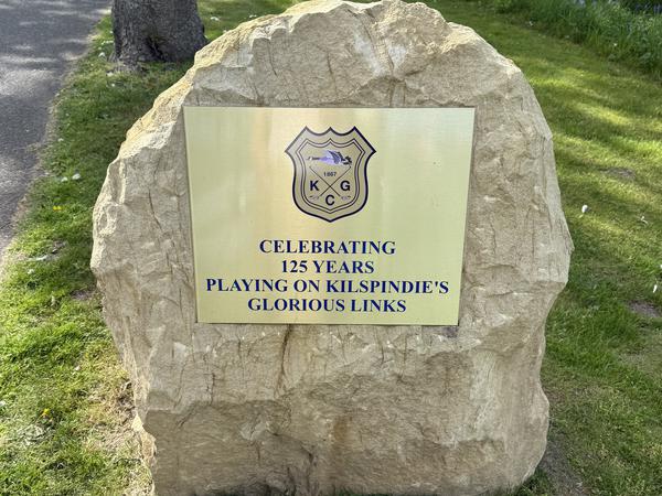 Schild auf einem Stein. Es steht darauf: Celebrating 125 Years Playing on Kilspindie’s Glorious Links