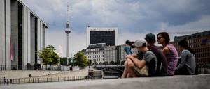Touristen sitzen am Spreeufer in der Nähe des Bundestags. Im Hintergrund ragt der Fernsehturm am Alexanderplatz in die Höhe. +++ dpa-Bildfunk +++