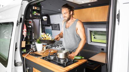 Ein Mann steht an der Küchenzeile seines Campingbusses.