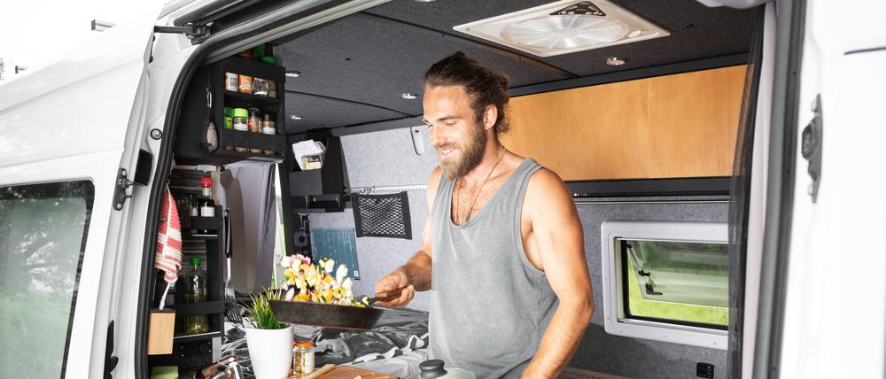 Ein Mann steht an der Küchenzeile seines Campingbusses.