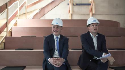 Kai Wegner, Regierender Bürgermeister von Berlin, und Ulrich Schiller, Geschäftsführung der landeseigenen Howoge, sitzen mit Schutzhelmen auf dem Kopf auf einer Baustelle nebeneinander