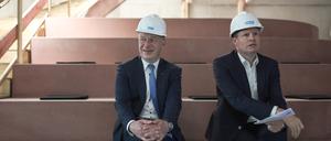 Kai Wegner, Regierender Bürgermeister von Berlin, und Ulrich Schiller, Geschäftsführung der landeseigenen Howoge, sitzen mit Schutzhelmen auf dem Kopf auf einer Baustelle nebeneinander