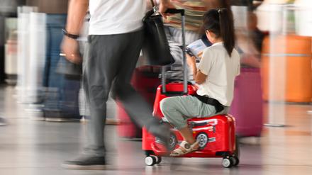 Ein Mädchen wird von seinem Vater auf ihrem Koffer durch das Terminal des Frankfurter Flughafens gezogen. 