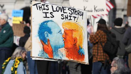 Ein Demonstrant hält ein Plakat, auf dem Donald Trump und Wladimir Putin abgebildet sind, die sich während einer Anti-Trump-Demonstration vor dem Pennsylvania State Capitol küssen.