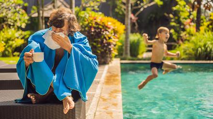 Ein Mann sitzt mit Taschentüchern und Tee an einem Pool.