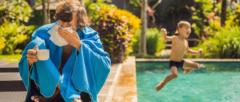 Ein Mann sitzt mit Taschentüchern und Tee an einem Pool.