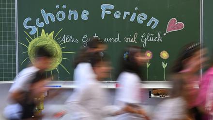 Schulkinder einer 4. Klasse einer Stuttgarter Grundschule laufen am letzten Schultag vor den Sommerferien in Baden-Württemberg an einer Tafel mit dem Aufschrieb: „Schöne Ferien Alles Gute und viel Glück“ vorbei.