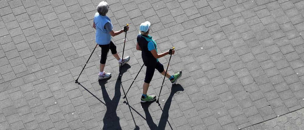 Zwei ältere Damen gehen mit Walking-Stöcken spazieren.