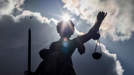 Eine Justitia-Statue steht im sonnigen Gegenlicht vor dunklen Wolken. (Symbolbild)