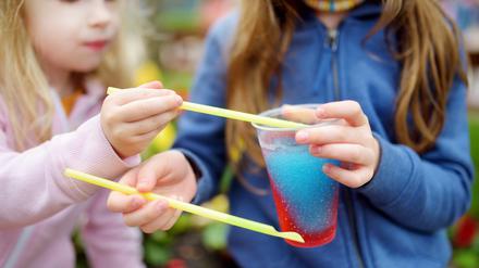 Zwei Mädchen löffeln buntes Slush-Eis aus einem Becher.