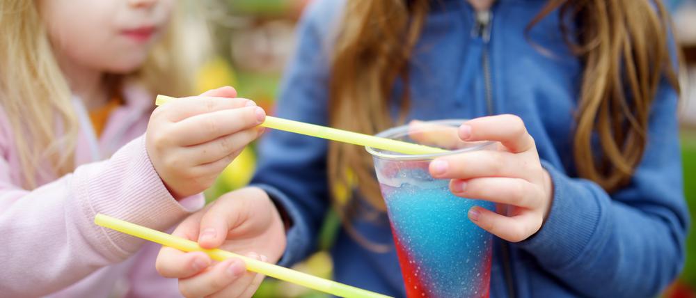 Zwei Mädchen löffeln buntes Slush-Eis aus einem Becher.