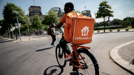 Ein Fahrradkurier des Essens-Lieferdienstes Lieferando fährt mit seinem Rucksack am Reichstagsgebäude in Berlin vorbei.