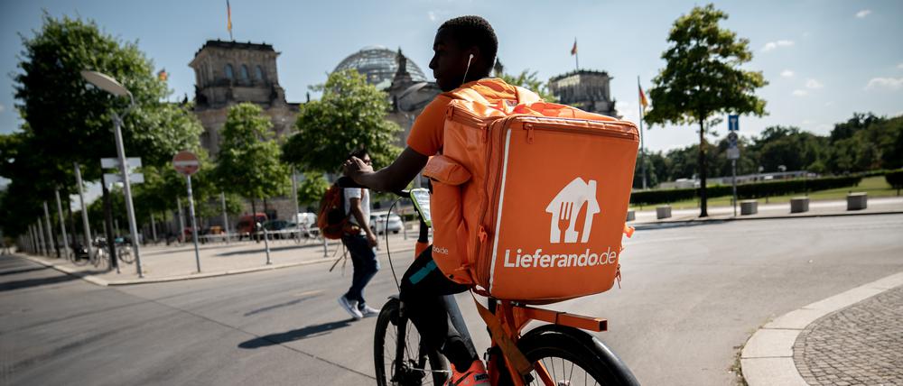 Ein Fahrradkurier des Essens-Lieferdienstes Lieferando fährt mit seinem Rucksack am Reichstagsgebäude in Berlin vorbei.