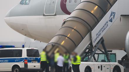 Menschen besteigen ein Flugzeug der Qatar Airways, vor dem Fahrzeuge der Bundespolizei stehen auf dem Vorfeld am Flughafen Leipzig/Halle.