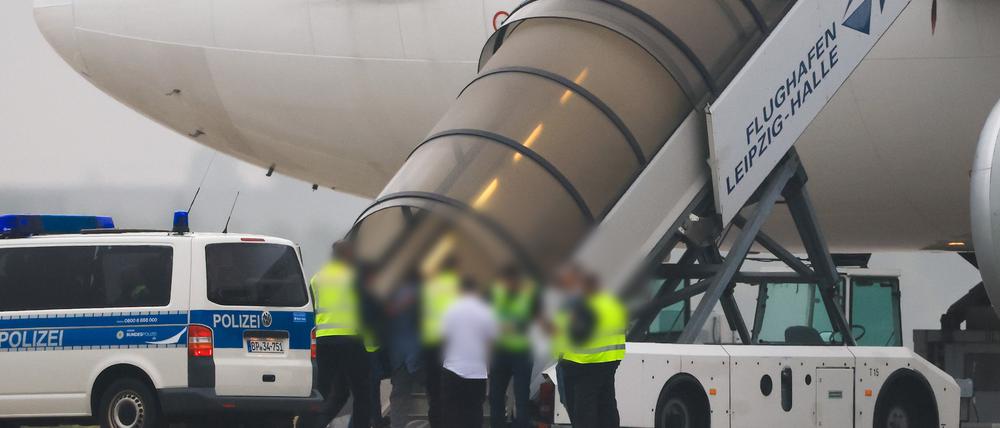 Menschen besteigen ein Flugzeug der Qatar Airways, vor dem Fahrzeuge der Bundespolizei stehen auf dem Vorfeld am Flughafen Leipzig/Halle.